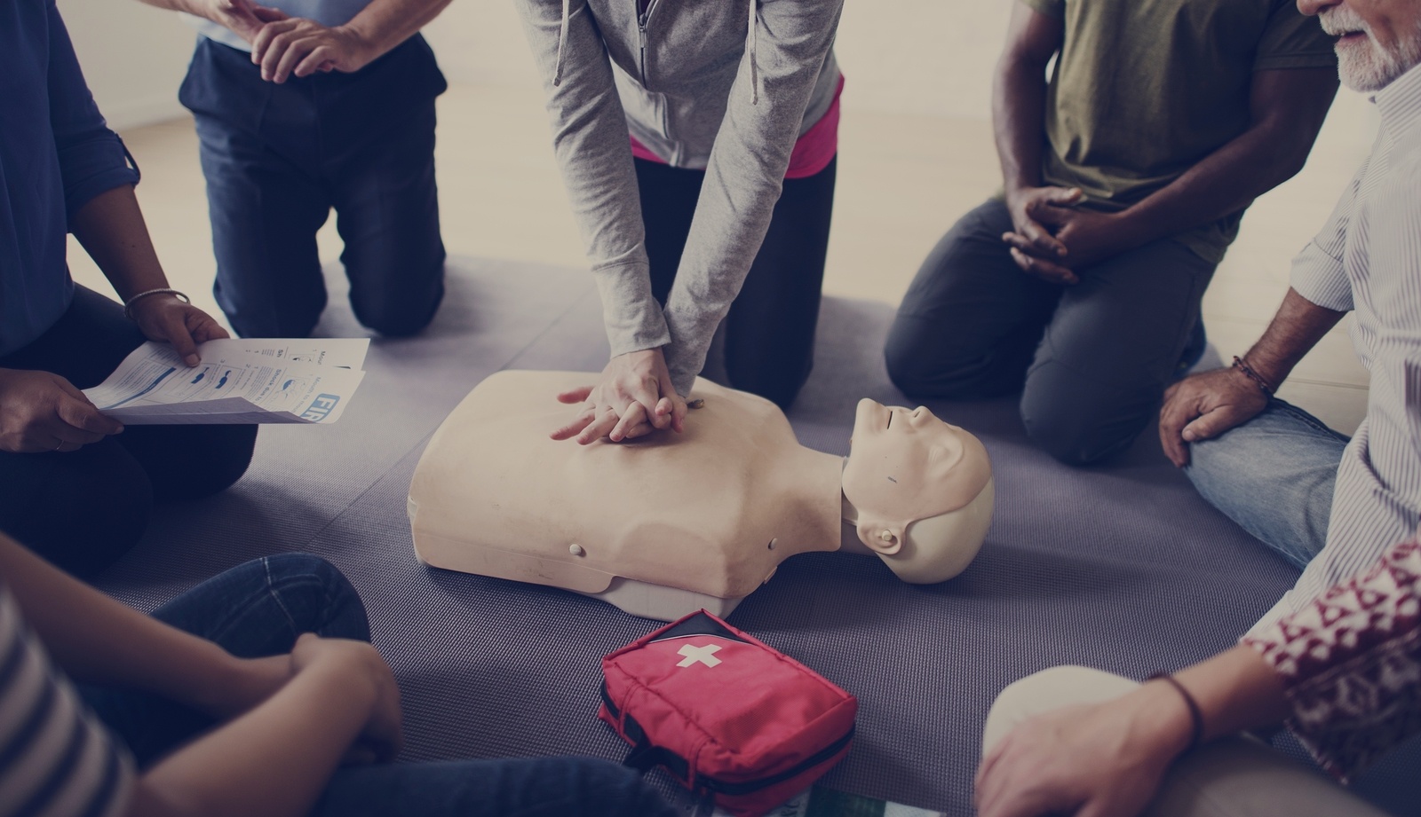 group of 5 people learning cpr from an instructor on a dummy